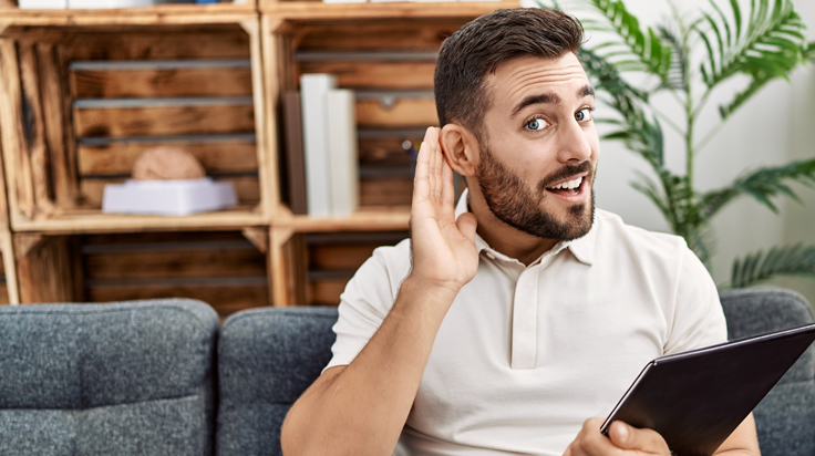 A smiling man trying to hear better by placing his hand behind his ear during a business meeting